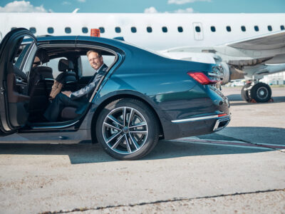 smiling-mature-businessman-in-car-near-plane-2023-11-27-05-21-55-utc (1)