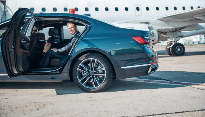 smiling-mature-businessman-in-car-near-plane-2023-11-27-05-21-55-utc (1)