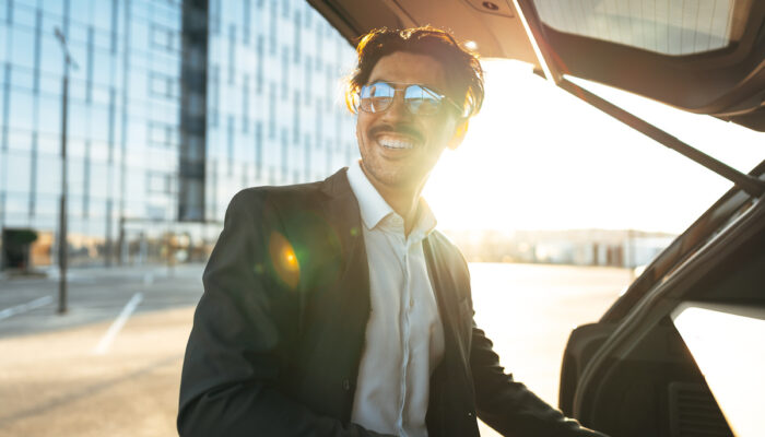 Successful businessman taking luggage from the car trunk