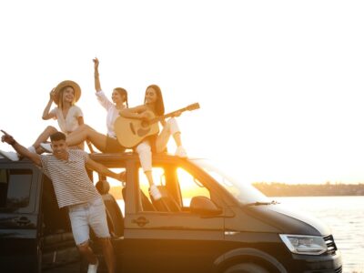 Happy friends with guitar near sea at sunset. Summer trip