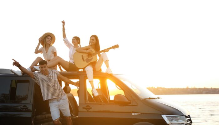 Happy friends with guitar near sea at sunset. Summer trip
