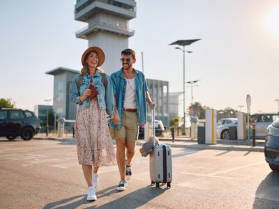 Happy couple with passports and suitcase going to airport terminal. Copy space.
