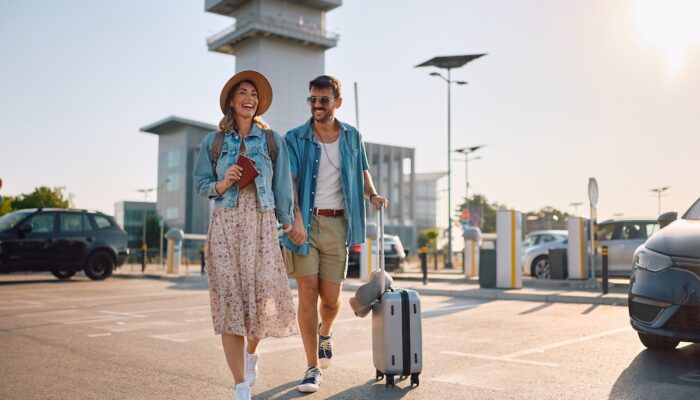 Happy couple with passports and suitcase going to airport terminal. Copy space.